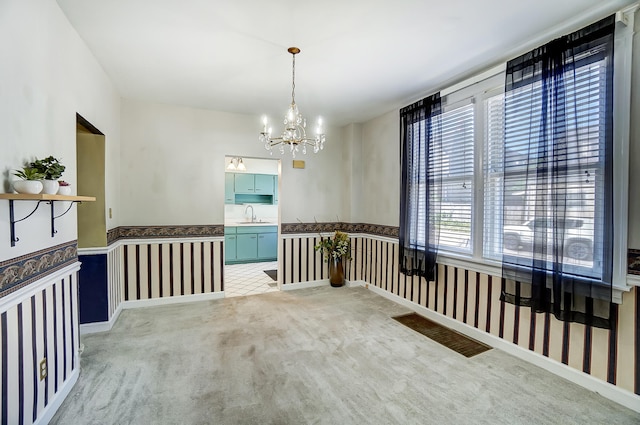 unfurnished room with wallpapered walls, an inviting chandelier, a sink, wainscoting, and light carpet