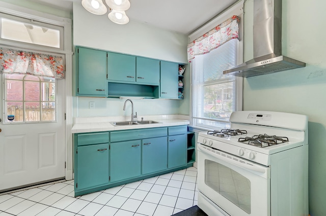 kitchen with white range with gas stovetop, a sink, light countertops, wall chimney exhaust hood, and a wealth of natural light