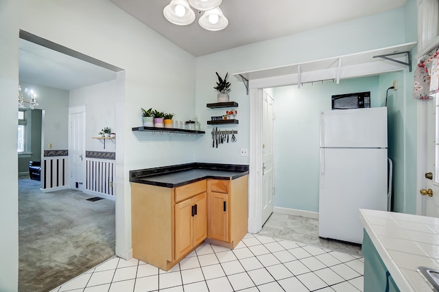 kitchen featuring tile countertops, freestanding refrigerator, black microwave, light carpet, and a notable chandelier