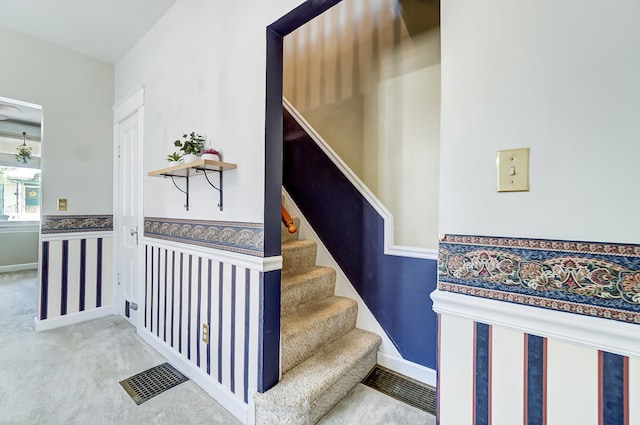 staircase with visible vents, carpet floors, baseboards, and a wainscoted wall