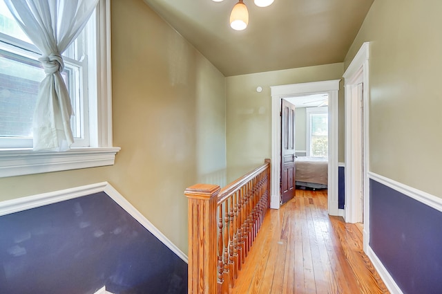 hall featuring baseboards, an upstairs landing, and light wood-style floors