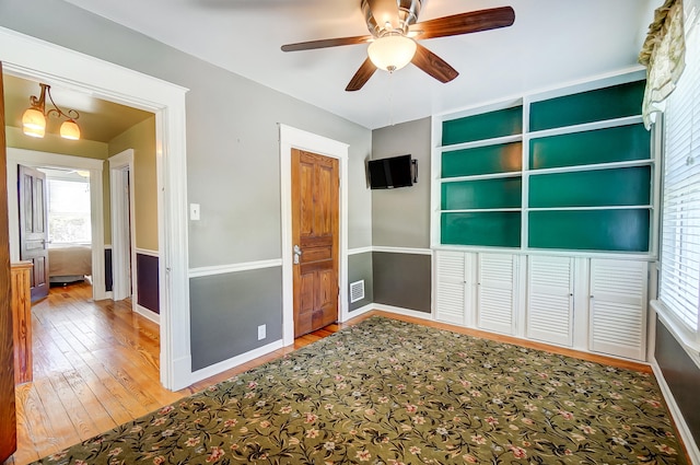 unfurnished bedroom with visible vents, multiple windows, baseboards, and hardwood / wood-style flooring