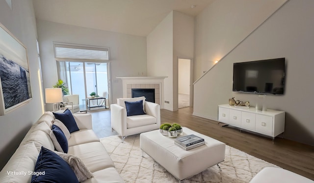 living area featuring a tiled fireplace, light wood-style floors, and a towering ceiling