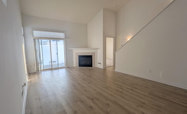 unfurnished living room featuring a tile fireplace, baseboards, a towering ceiling, and wood finished floors