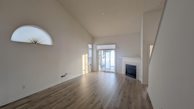 unfurnished living room featuring visible vents, baseboards, a tile fireplace, wood finished floors, and high vaulted ceiling