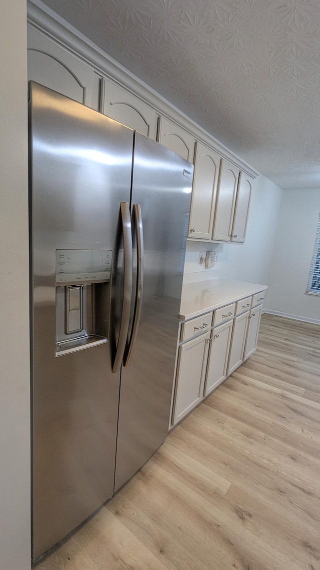 kitchen with light countertops, stainless steel fridge with ice dispenser, light wood finished floors, and a textured ceiling