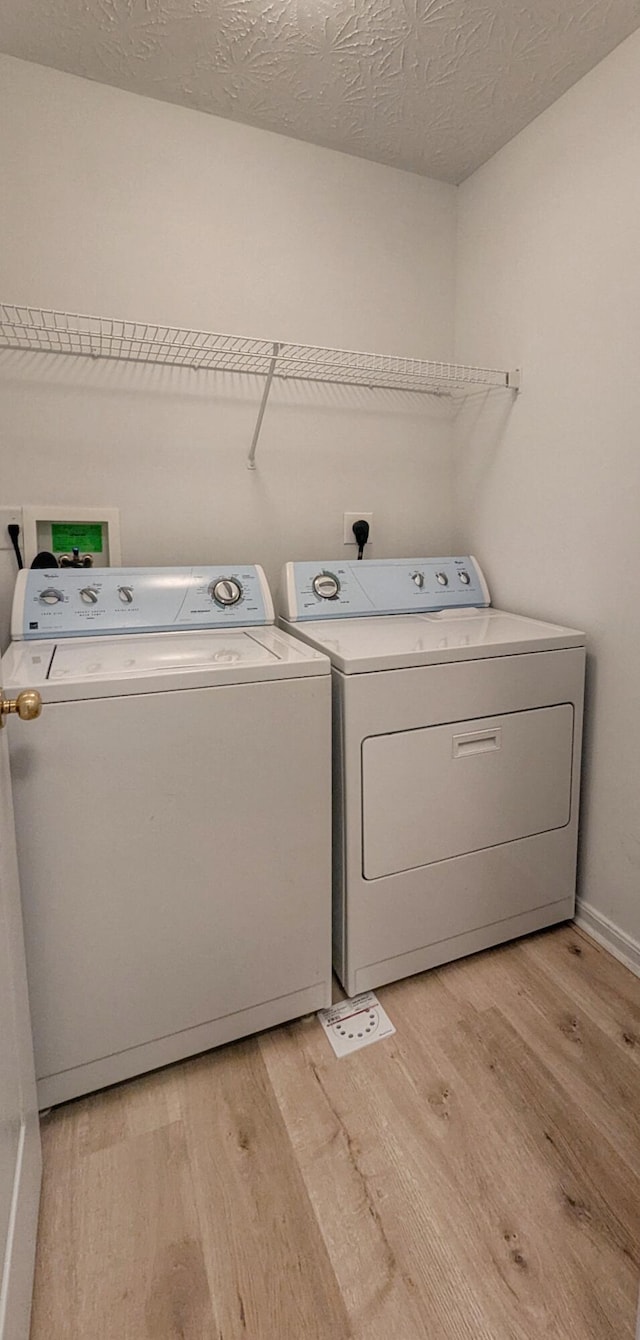 laundry area featuring a textured ceiling, light wood-style flooring, laundry area, and washing machine and clothes dryer