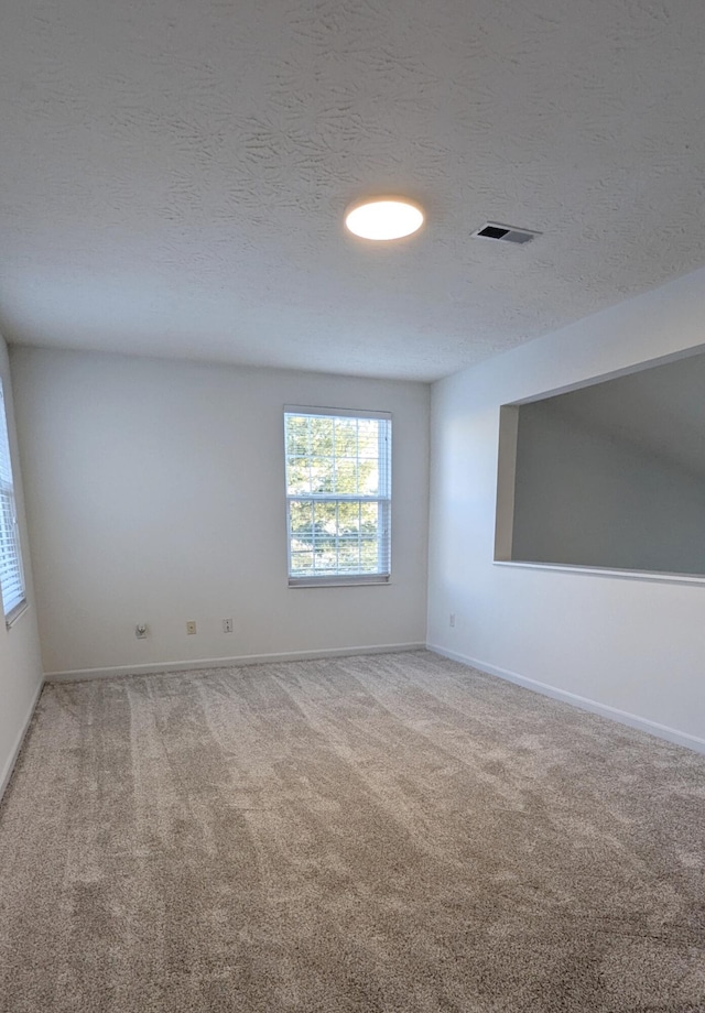 empty room featuring visible vents, light carpet, a textured ceiling, and baseboards