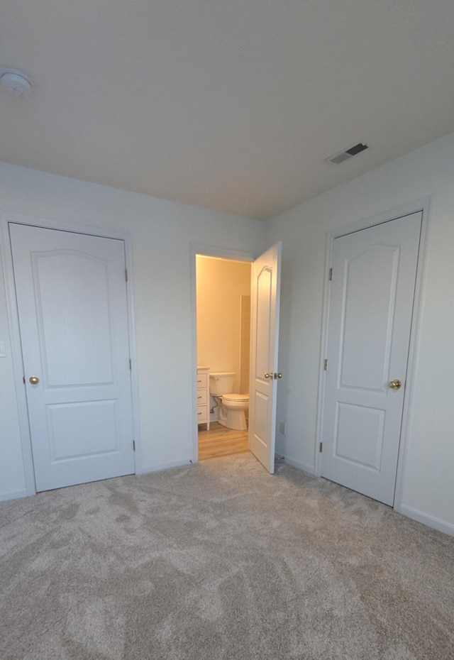 unfurnished bedroom featuring carpet flooring, baseboards, visible vents, and ensuite bathroom