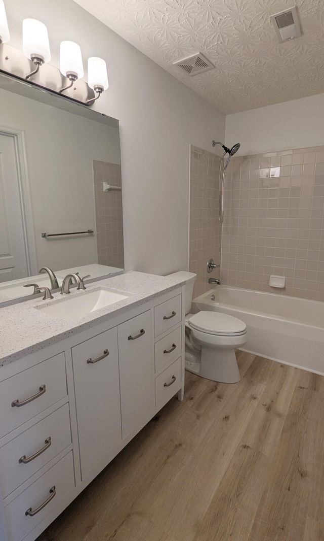 full bath featuring visible vents, washtub / shower combination, toilet, wood finished floors, and a textured ceiling