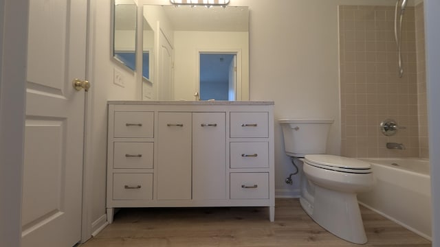 bathroom with vanity, wood finished floors, baseboards,  shower combination, and toilet