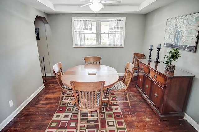 dining space with dark wood-style floors, baseboards, a raised ceiling, and a ceiling fan