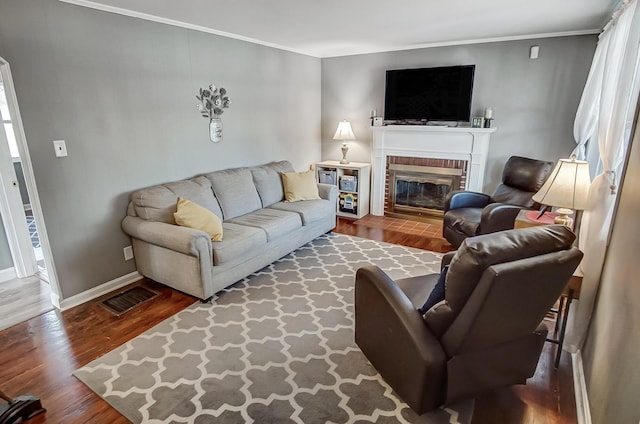 living room featuring visible vents, a brick fireplace, crown molding, baseboards, and wood finished floors