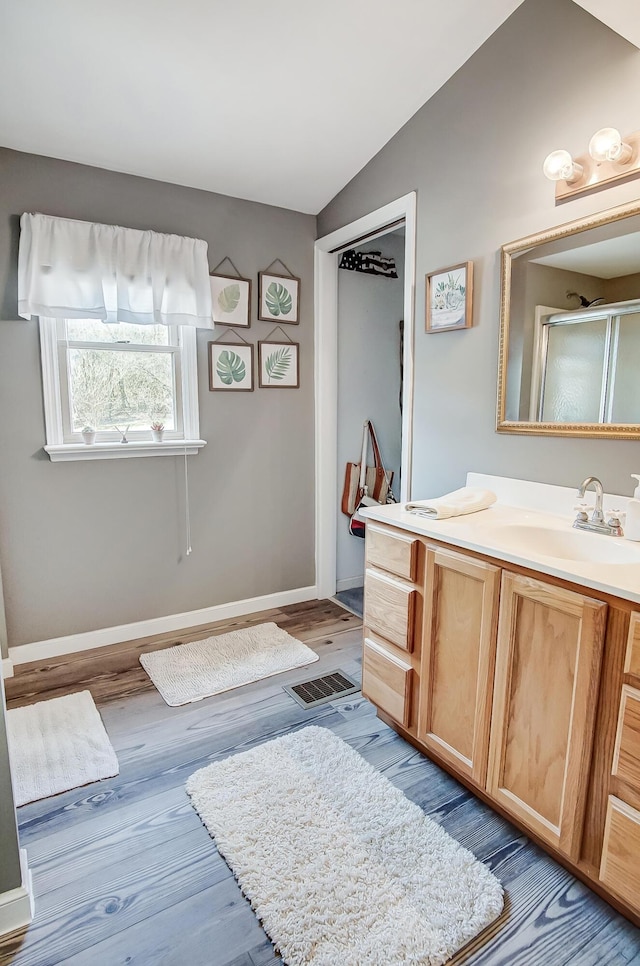 bathroom featuring vanity, wood finished floors, baseboards, vaulted ceiling, and a shower stall