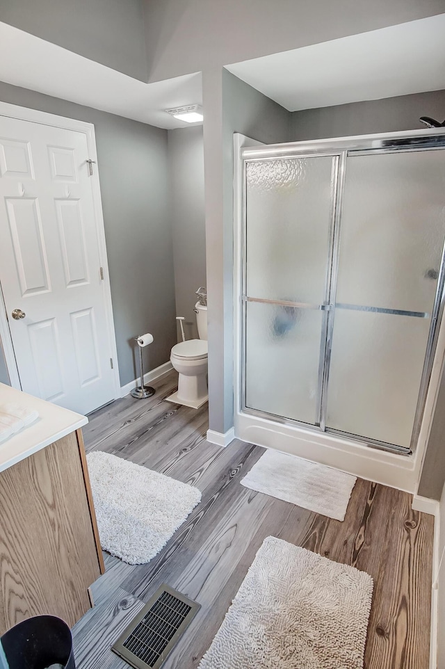 bathroom with a shower with door, visible vents, baseboards, toilet, and wood finished floors