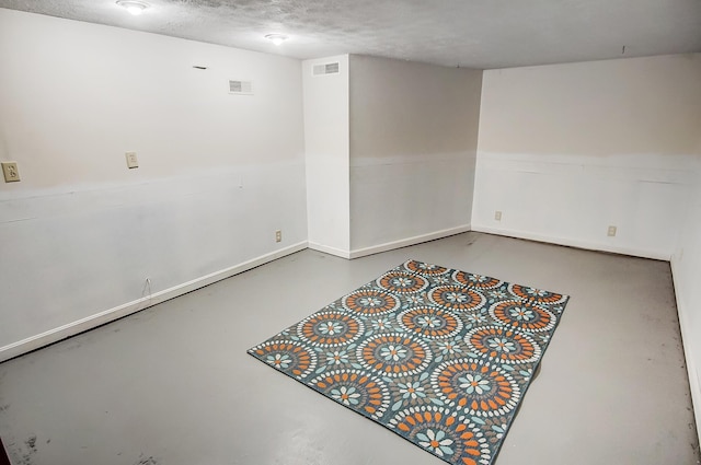 below grade area with visible vents, a textured ceiling, and baseboards