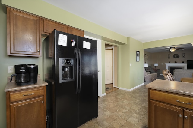 kitchen featuring ceiling fan, baseboards, open floor plan, a fireplace, and black fridge with ice dispenser