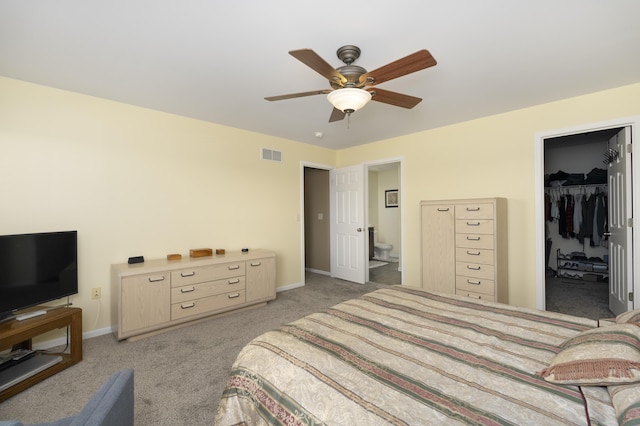 bedroom featuring baseboards, visible vents, ensuite bath, light carpet, and a walk in closet