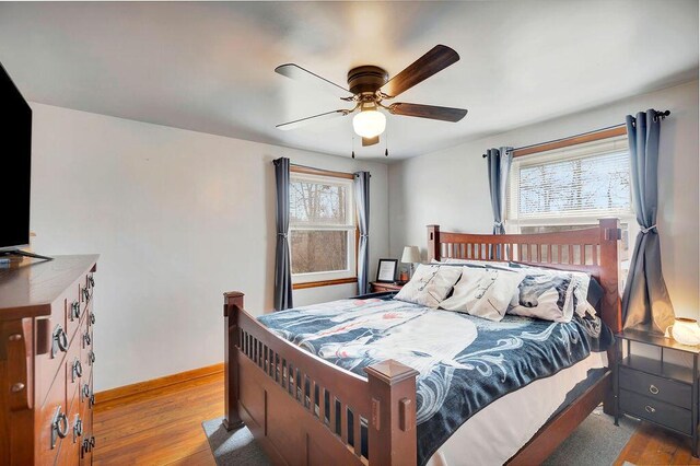 bedroom featuring baseboards, multiple windows, wood finished floors, and a ceiling fan