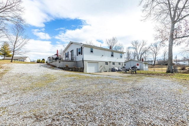 rear view of property with a chimney, gravel driveway, and an attached garage