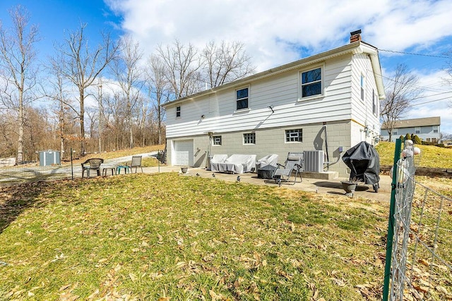 rear view of property featuring a patio, an attached garage, a chimney, central air condition unit, and a lawn