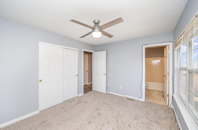 unfurnished bedroom with ensuite bath, carpet flooring, a closet, a textured ceiling, and a ceiling fan