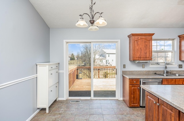 kitchen featuring brown cabinetry, visible vents, a sink, stainless steel dishwasher, and a notable chandelier