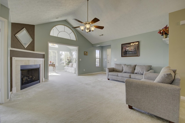 carpeted living room featuring visible vents, a tile fireplace, a textured ceiling, high vaulted ceiling, and a ceiling fan