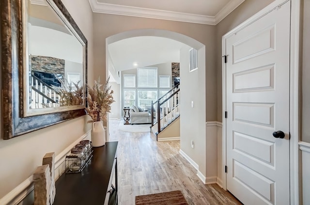 foyer entrance featuring crown molding, baseboards, stairs, wood finished floors, and arched walkways