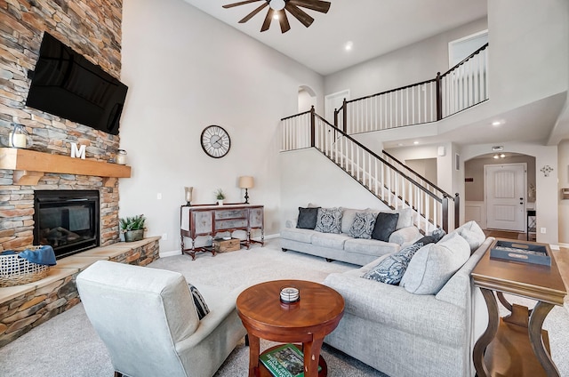 living area featuring a towering ceiling, stairway, arched walkways, a fireplace, and ceiling fan