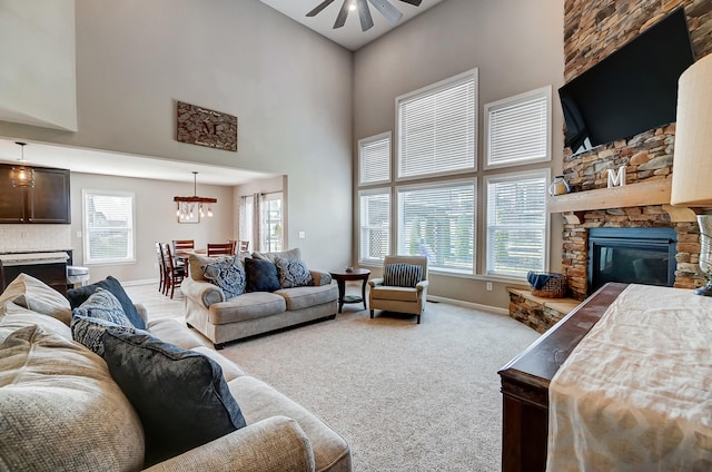 carpeted living room with a wealth of natural light, a stone fireplace, and ceiling fan with notable chandelier