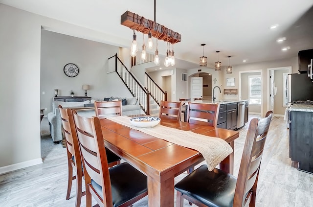 dining room featuring light wood-type flooring, recessed lighting, arched walkways, baseboards, and stairs