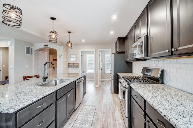 kitchen featuring visible vents, decorative backsplash, arched walkways, stainless steel appliances, and a sink