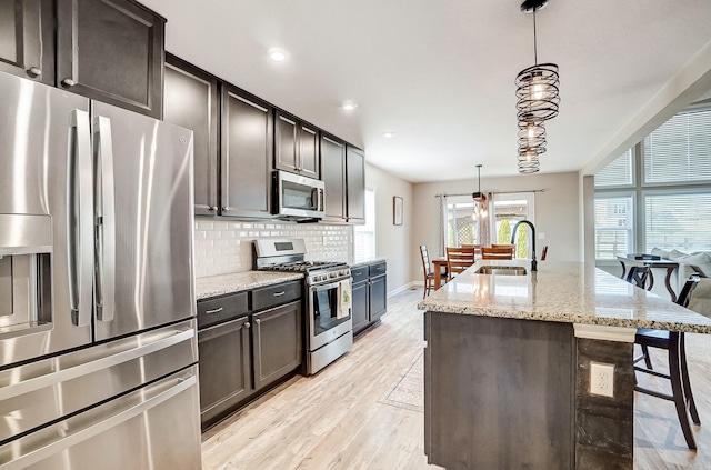 kitchen featuring light wood-type flooring, a sink, tasteful backsplash, appliances with stainless steel finishes, and light stone countertops