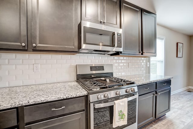 kitchen featuring baseboards, light stone counters, decorative backsplash, light wood-style flooring, and appliances with stainless steel finishes