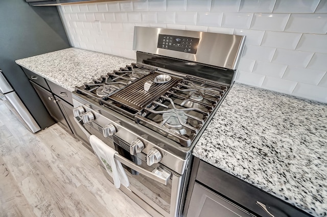 room details featuring stainless steel gas stove, light wood-style flooring, tasteful backsplash, fridge, and light stone countertops