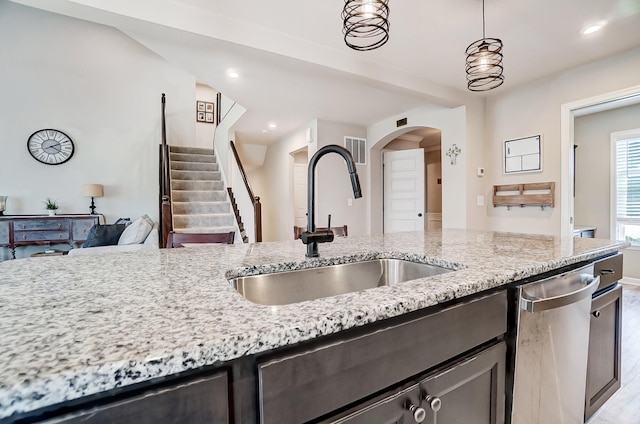 kitchen with arched walkways, a sink, light stone countertops, and stainless steel dishwasher