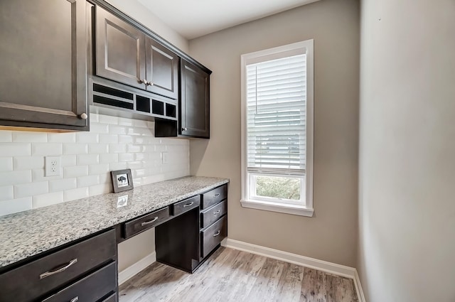 kitchen featuring tasteful backsplash, baseboards, dark brown cabinetry, light stone counters, and light wood-style flooring