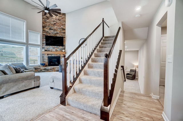 stairway featuring baseboards, a fireplace, a high ceiling, wood finished floors, and a ceiling fan