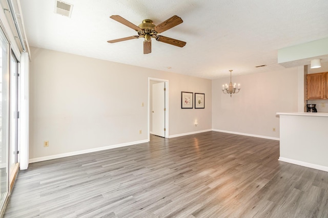 spare room with visible vents, light wood finished floors, baseboards, a textured ceiling, and ceiling fan with notable chandelier