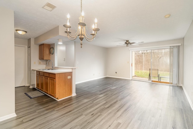 kitchen with ceiling fan with notable chandelier, a sink, wood finished floors, brown cabinetry, and light countertops