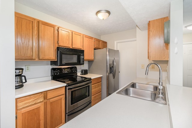 kitchen with a textured ceiling, light countertops, appliances with stainless steel finishes, and a sink