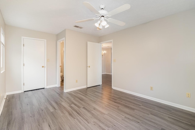 unfurnished bedroom featuring visible vents, baseboards, wood finished floors, and ceiling fan with notable chandelier