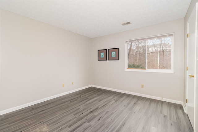 spare room with visible vents, baseboards, a textured ceiling, and wood finished floors