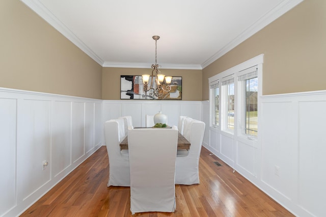 dining room with crown molding, a decorative wall, wood finished floors, and a chandelier