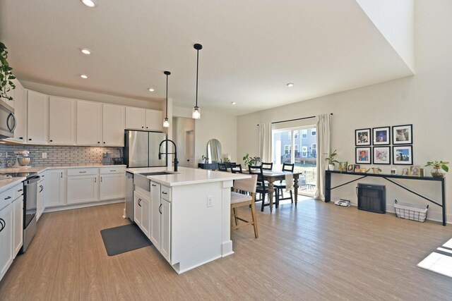 kitchen featuring light wood-type flooring, a sink, tasteful backsplash, appliances with stainless steel finishes, and light countertops