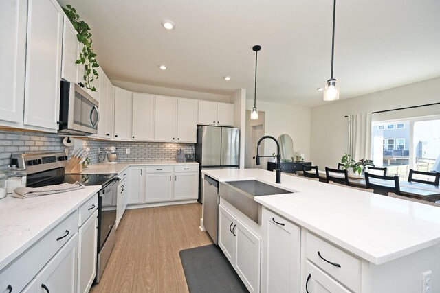 kitchen with a sink, stainless steel appliances, white cabinetry, light wood-type flooring, and backsplash