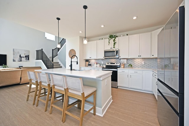 kitchen with light wood finished floors, open floor plan, a kitchen bar, appliances with stainless steel finishes, and a sink