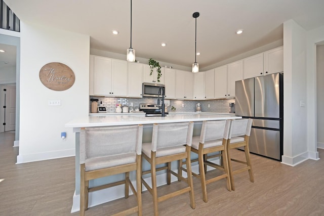 kitchen with light wood-style flooring, tasteful backsplash, white cabinetry, appliances with stainless steel finishes, and light countertops