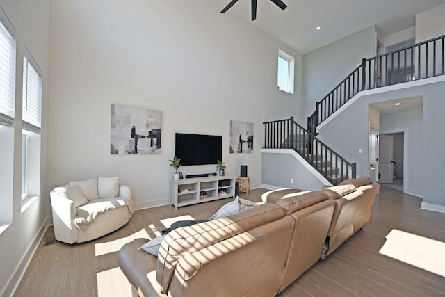 living area with stairway, baseboards, a towering ceiling, and wood finished floors